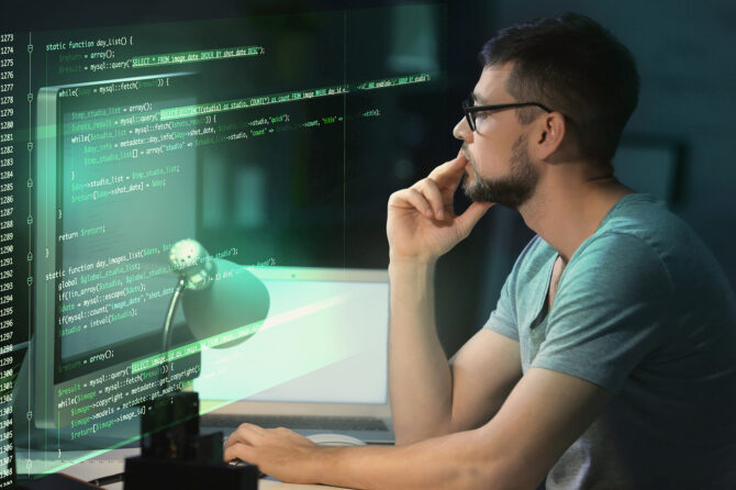 Computer programmer pondering lines of code on an oversized monitor.