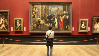 Person standing in front of museum wall displaying framed paintings.