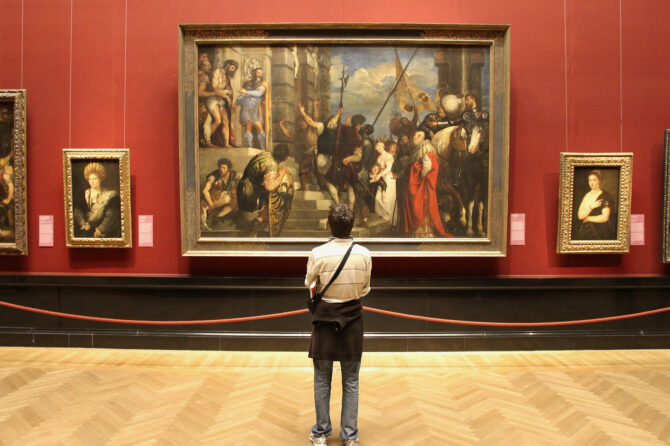 Person standing in front of museum wall displaying framed paintings.