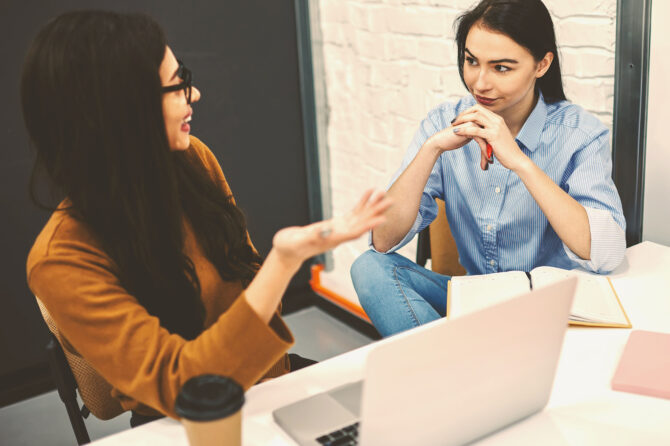 Two young business people in a discussion at a desk.