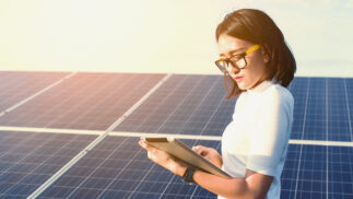 Scientist examining a tablet in front of solar panels.