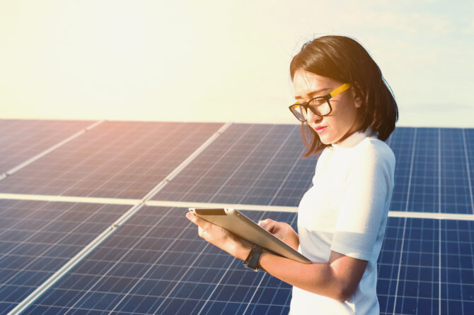 Scientist examining a tablet in front of solar panels.