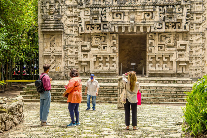 Four tourists at a Maya temple taking pictures and viewing the relief.