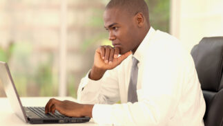 Young adult wearing a shirt and tie looking thoughtfully at a notebook computer.