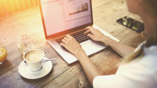 Person creating content on a notebook computer in a coffee shop.