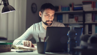 Person writing a paper on a notebook computer using a literary source as a reference.