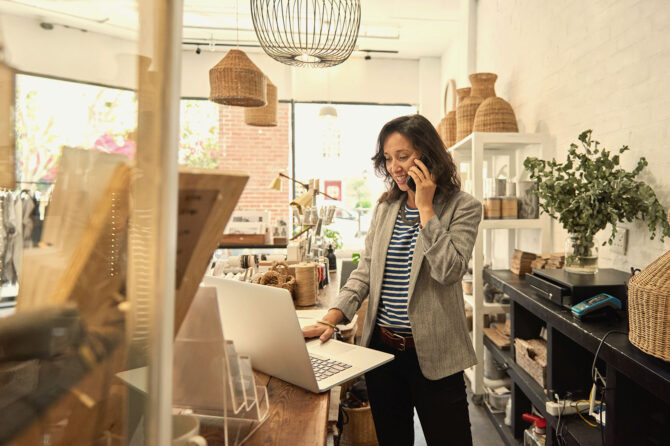 Small business owner working on a computer and speaking on the phone in a store.