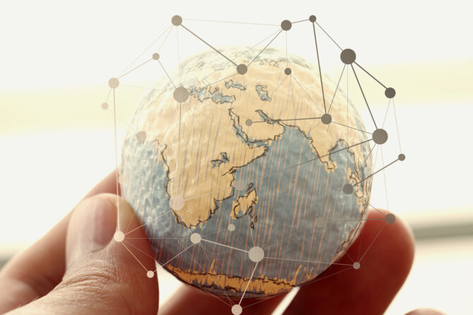 Hand holding a small globe with superimposed network showing connections.