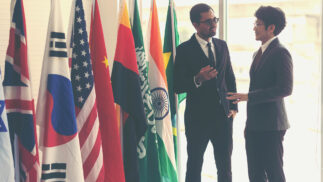 Two men speaking in front of a number of countries' flags.