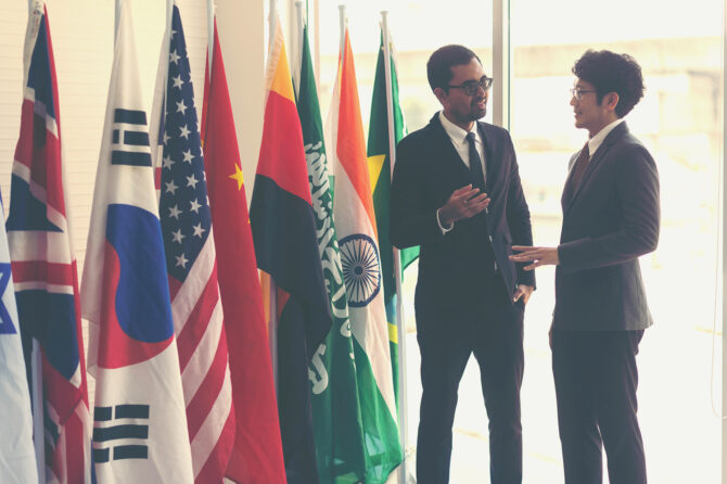 Two men speaking in front of a number of countries' flags.