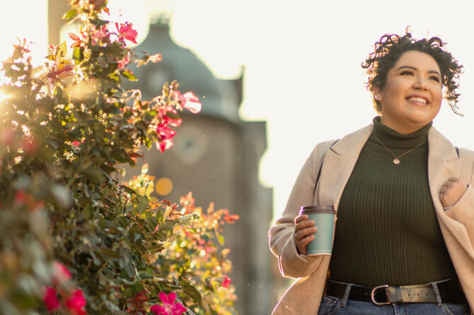 Smiling woman with coffee cup on a college campus.