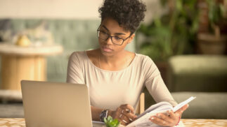 Person reviewing information on a notebook computer while looking at a text book.