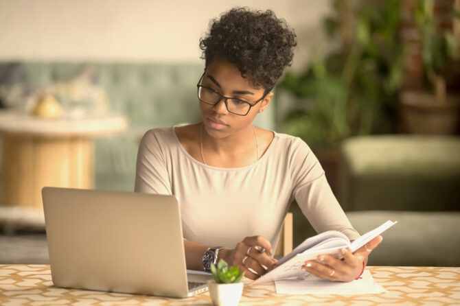 Person reviewing information on a notebook computer while looking at a text book.