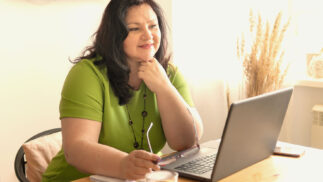 A woman sits in front of a laptop, looking thoughtful.