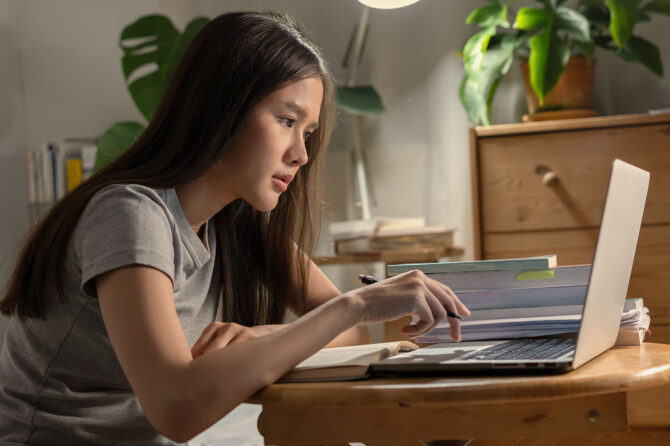 A woman sits hunched over a laptop on a small desk.