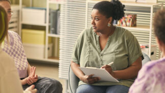A woman takes notes while listening to someone speak.